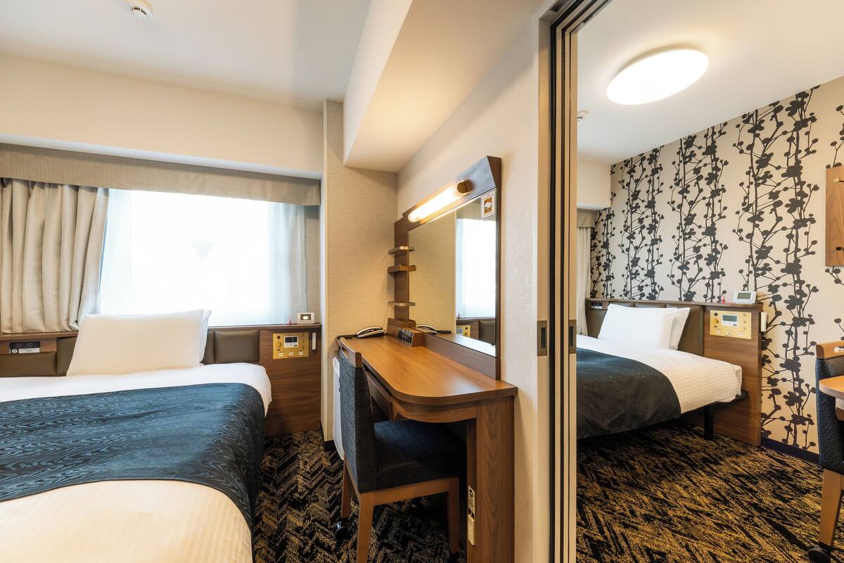 Ein Hotelzimmer mit zwei Betten, einem Schreibtisch, einem Spiegel und einem kleinen Tisch.