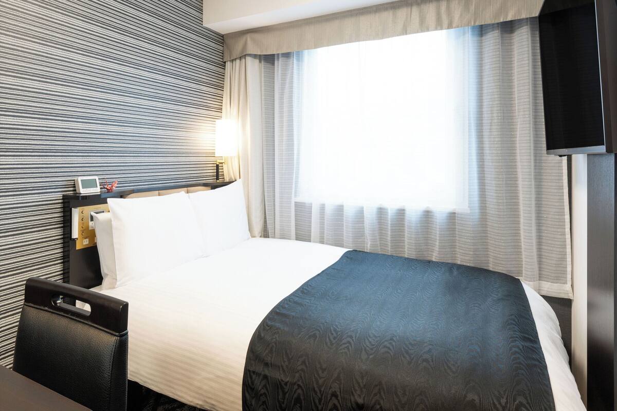 Ein Hotelzimmer mit Bett, Nachttisch, Lampe und einem an der Wand befestigten Fernseher.