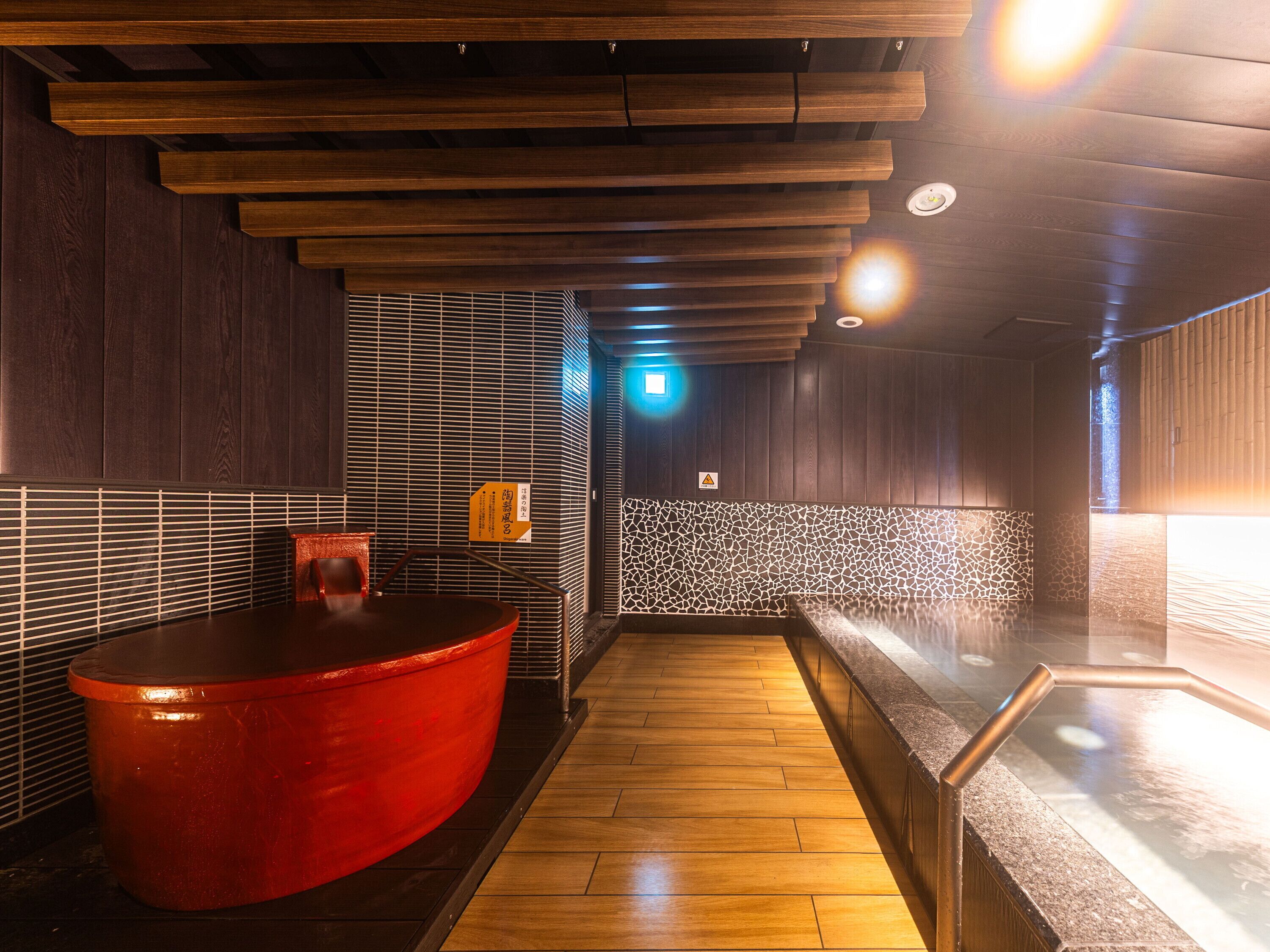 A spa area with a wooden ceiling, a red bathtub, and a tiled wall.