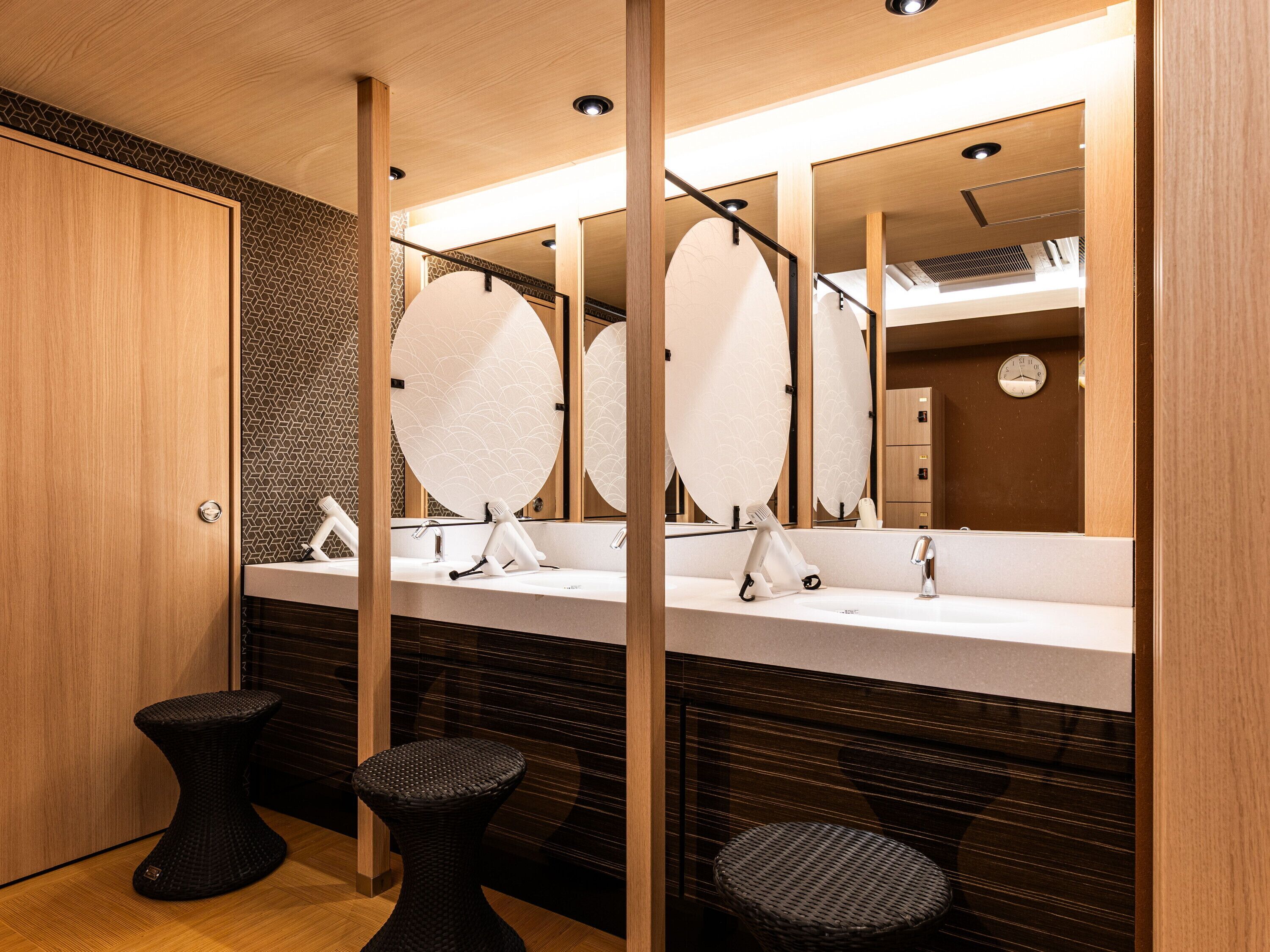 Une salle de bain moderne avec deux lavabos, des miroirs et des tabourets noirs.