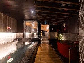 Un couloir doté d’un plancher en bois, d’une cloison en verre et d’un espace détente avec des sièges rouges.
