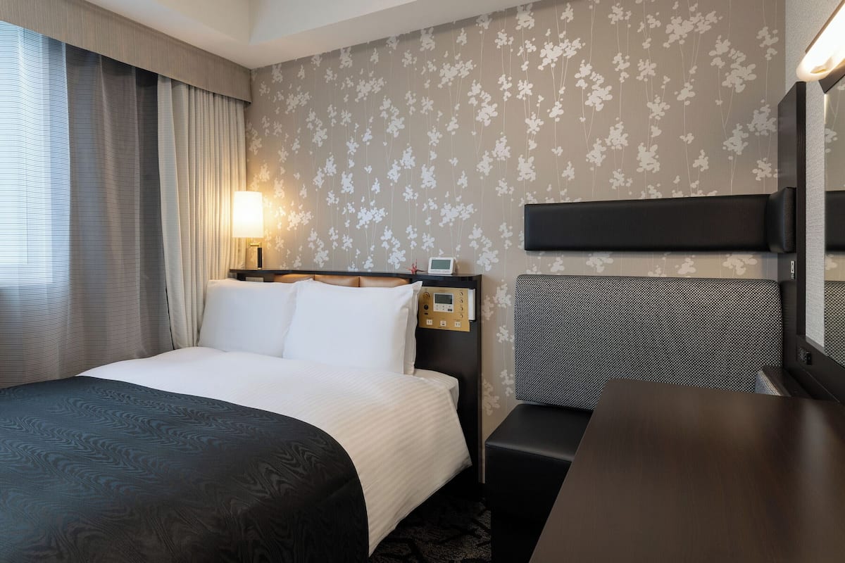 A hotel room with a bed, bedside table, lamp, and a wall-mounted TV.