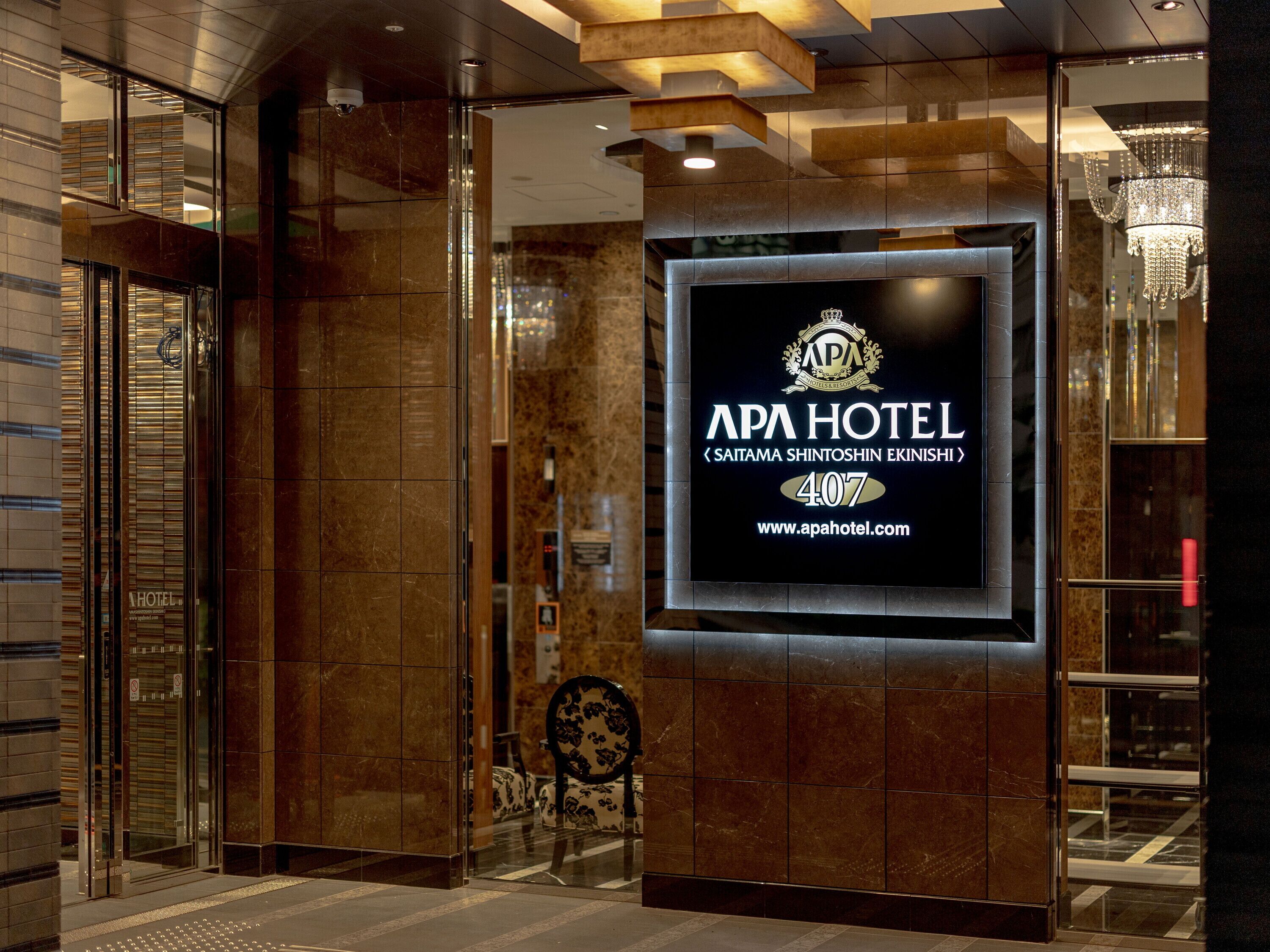 A modern hotel entrance with a large sign displaying the name 'APA HOTEL' and a website address.