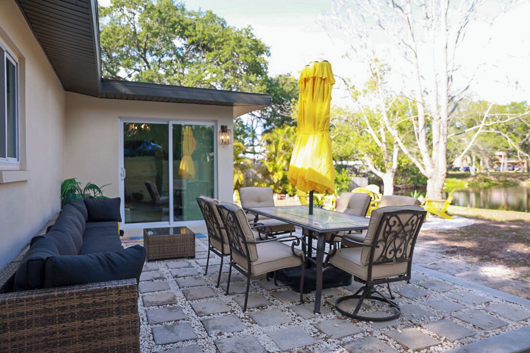 A patio with a dining table, chairs, and a yellow umbrella.