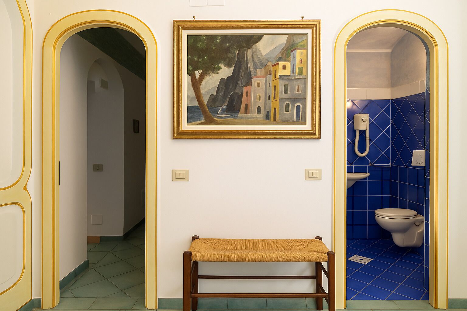 A hallway with a bench, a painting, and a bathroom with blue tiles.