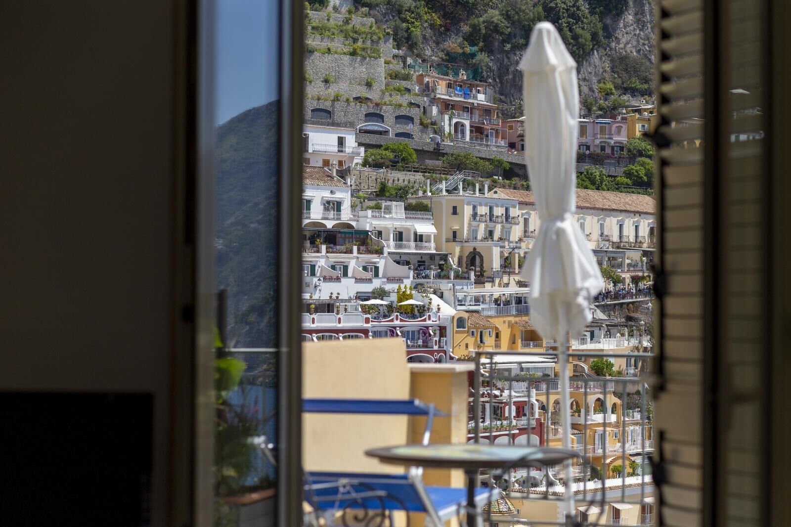 Vista di una cittadina costiera con edifici su una collina, una barca ormeggiata vicino alla riva e un ombrellone bianco in primo piano.