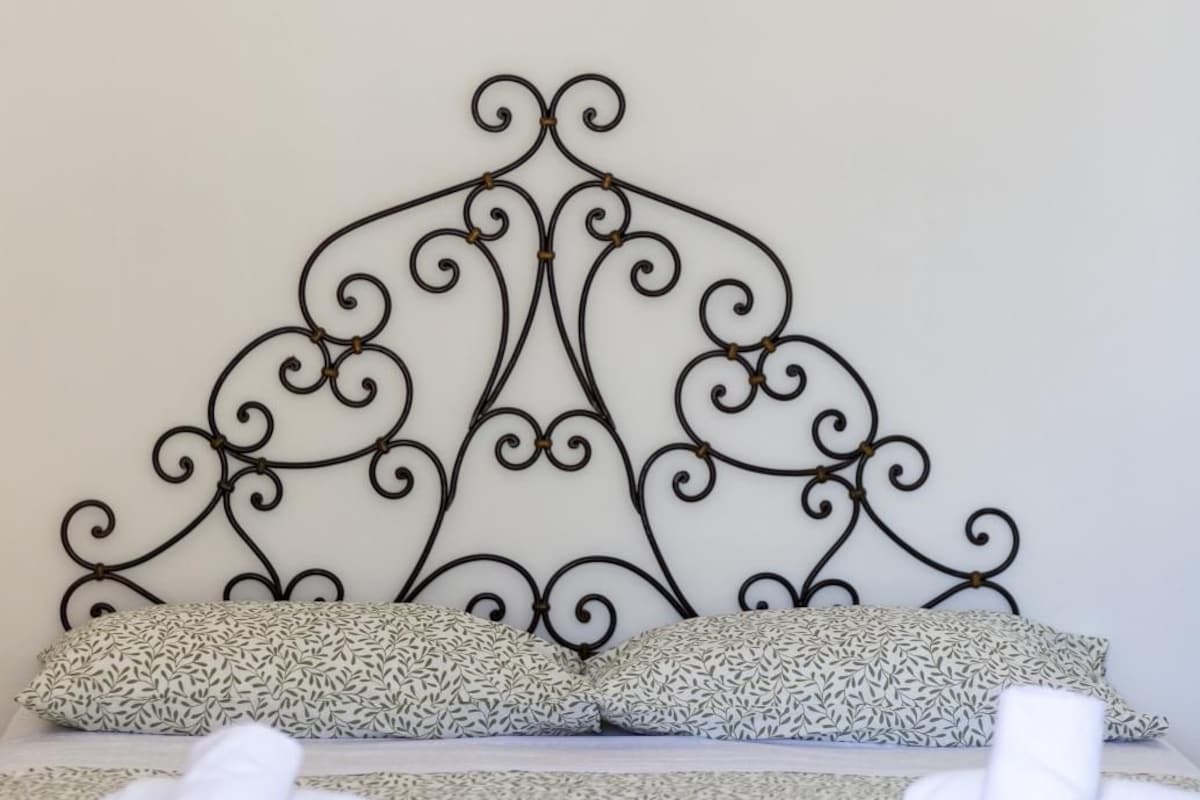 Un letto con testiera in metallo decorata, un cuscino a fantasia e asciugamani bianchi arrotolati su una coperta grigia con trama.