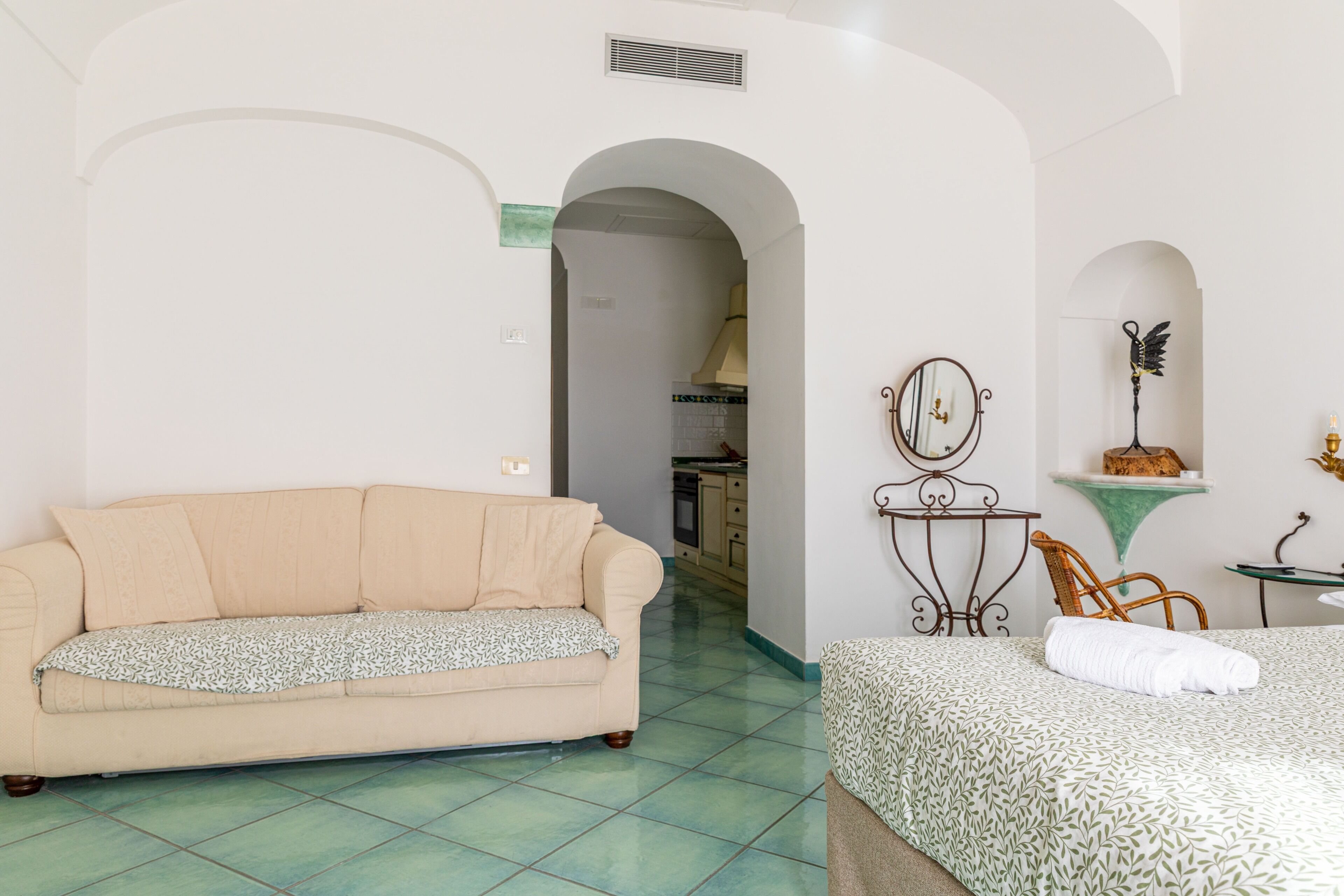 Una habitación con sofá, cama, mesita de noche con espejo y una silla.