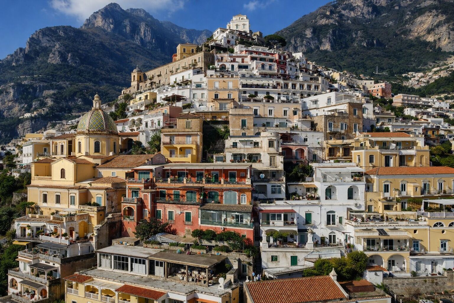 A densely packed hillside town with buildings closely built together, featuring a prominent church with a dome and bell tower.