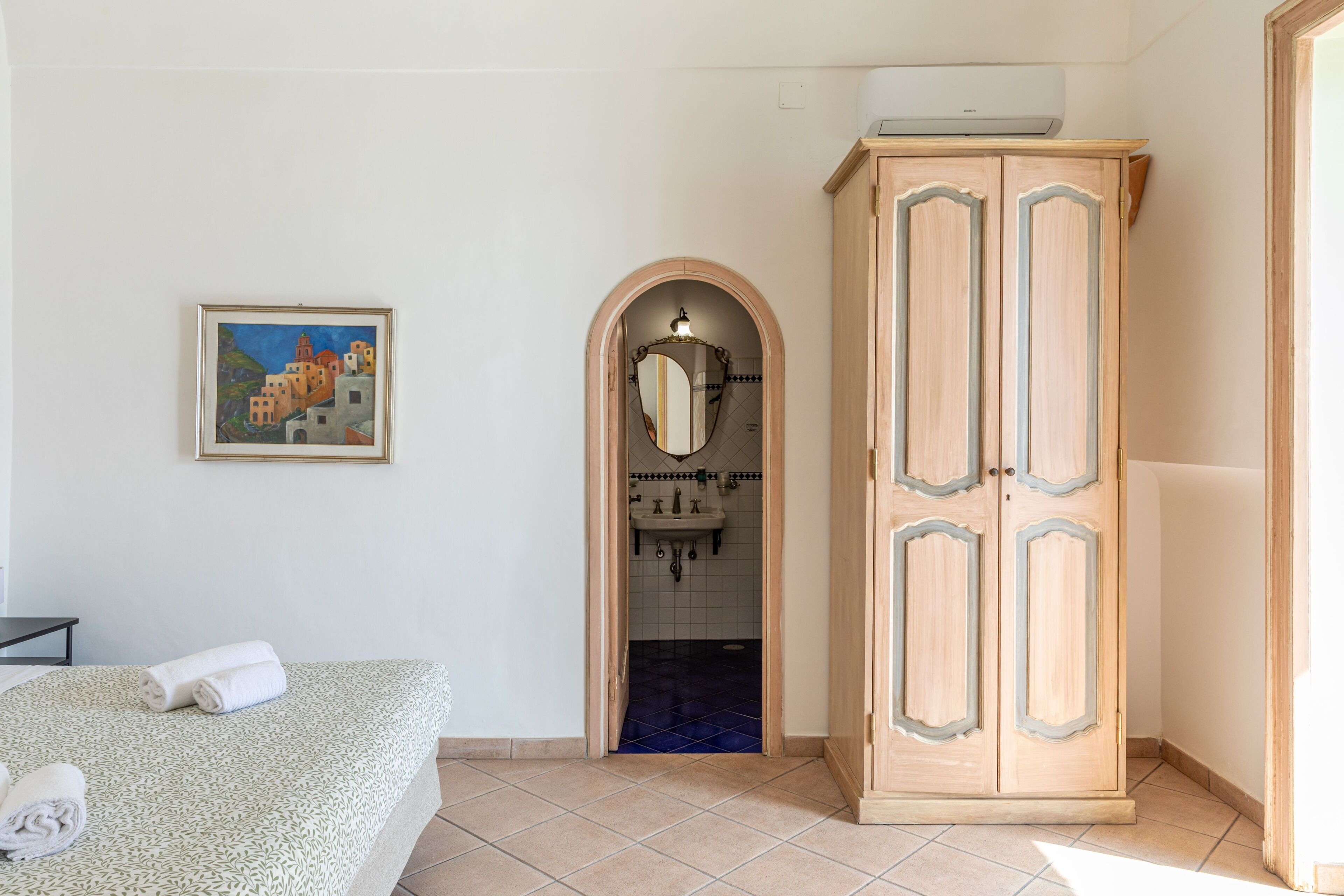 Een slaapkamer met een bed, een kledingkast, een badkamer met een wastafel en een schilderij aan de muur.