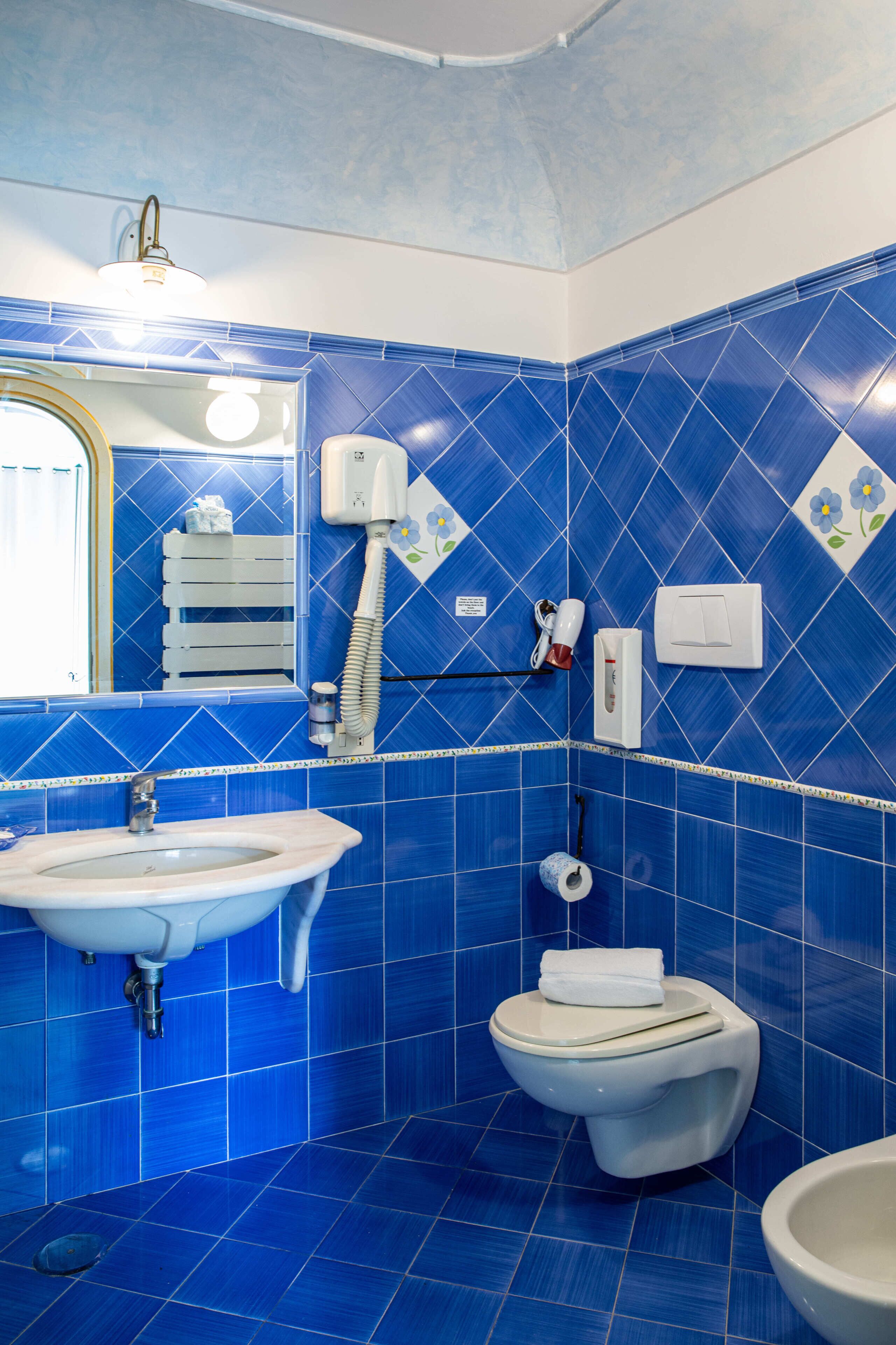 Un baño con azulejos azules, un lavamanos, un inodoro, un espejo y un perchero para toallas.