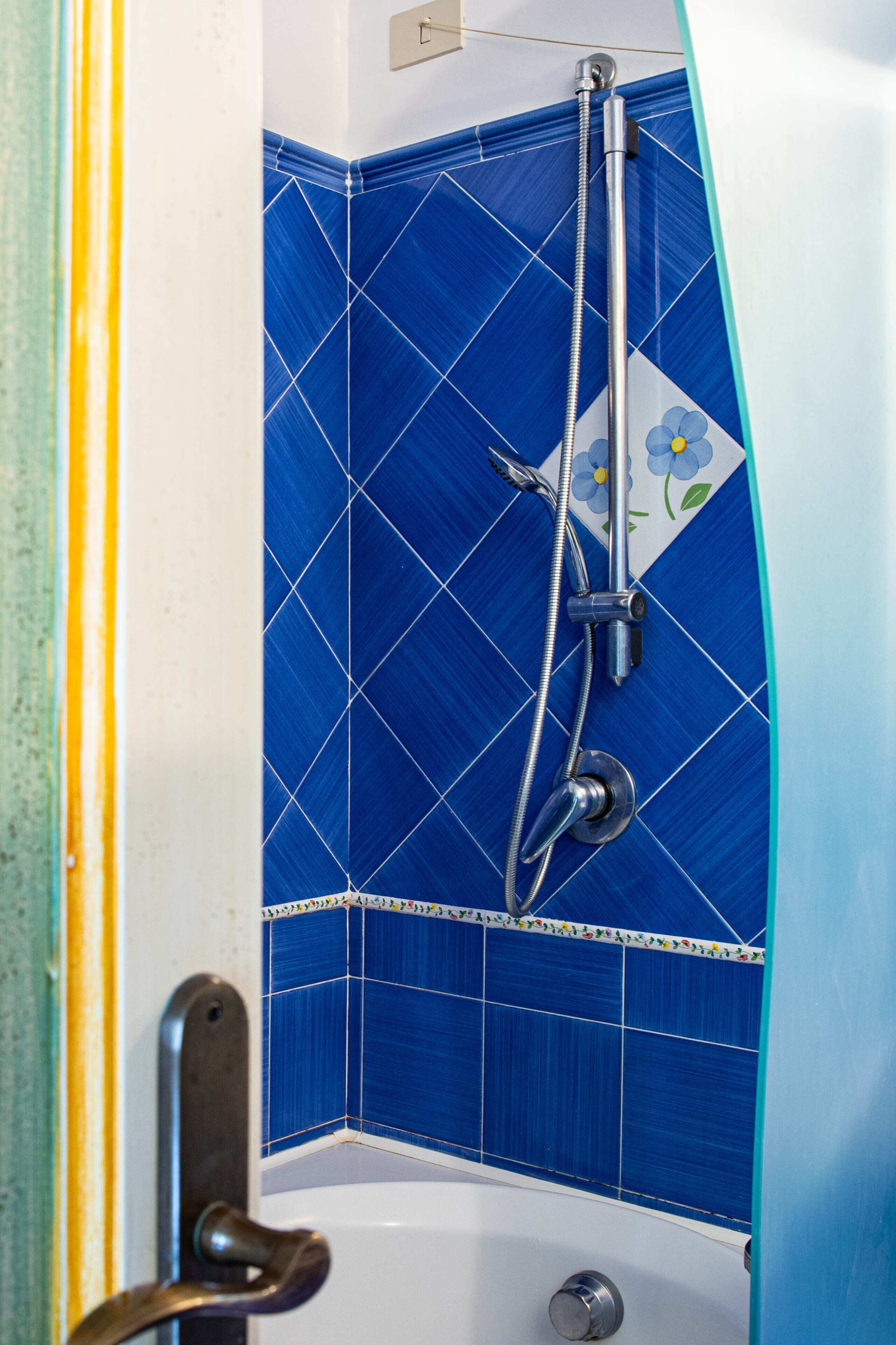 A corner of a bathroom with blue tiles, a showerhead, and a bathtub.