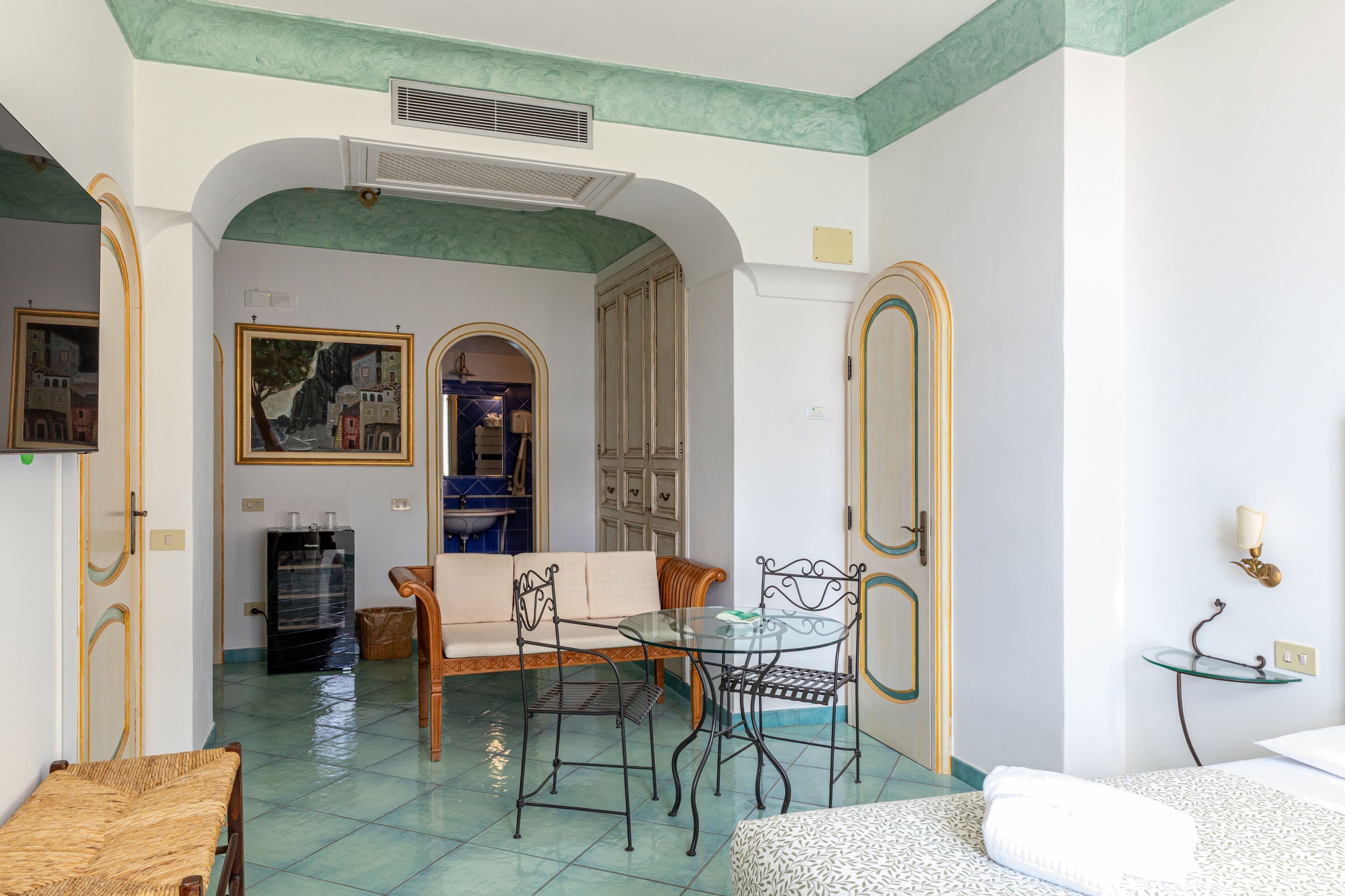 A room with a dining area, a sofa, a bed, and a bathroom visible through an archway.