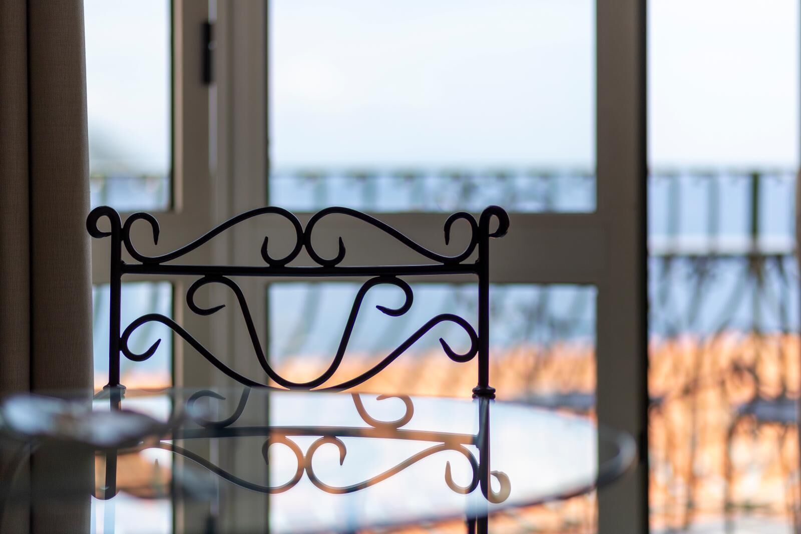 A metal chair with a decorative backrest in front of a window with a view of a balcony.