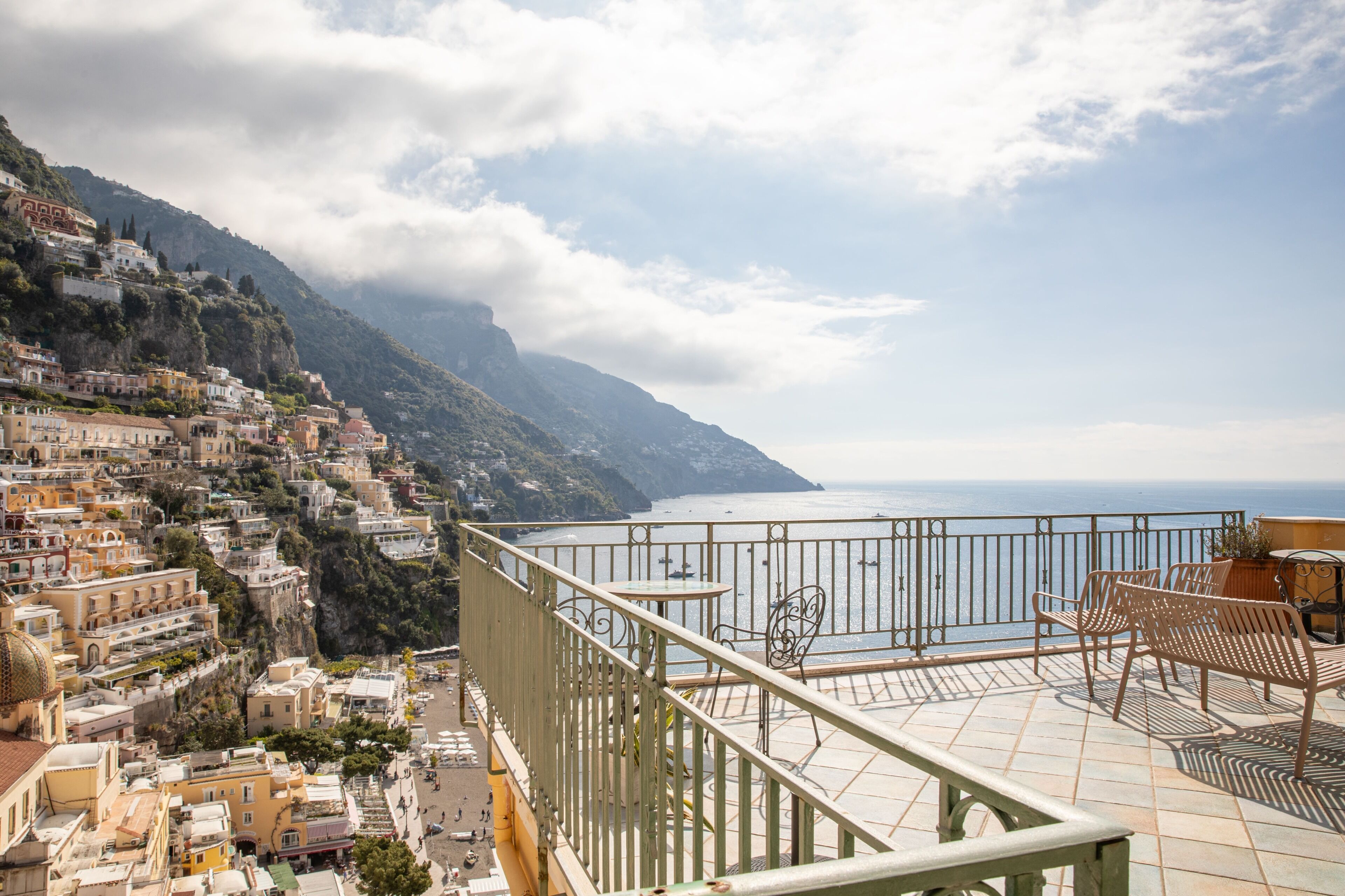 Una terraza con vistas a un pueblo costero, barandilla y mobiliario exterior.
