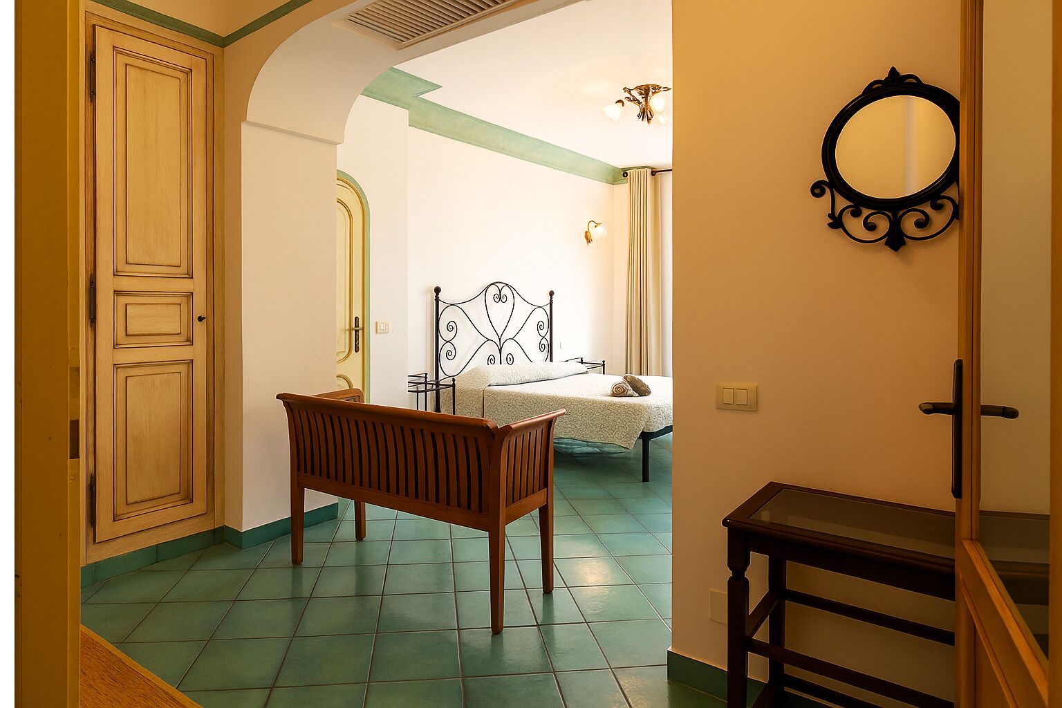 Une chambre à coucher avec un banc en bois, un lit doté d’une tête de lit décorative et un miroir au mur.