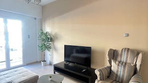 Una sala de estar moderna con un sofá, un sillón a rayas, una mesita y un televisor sobre un soporte negro.