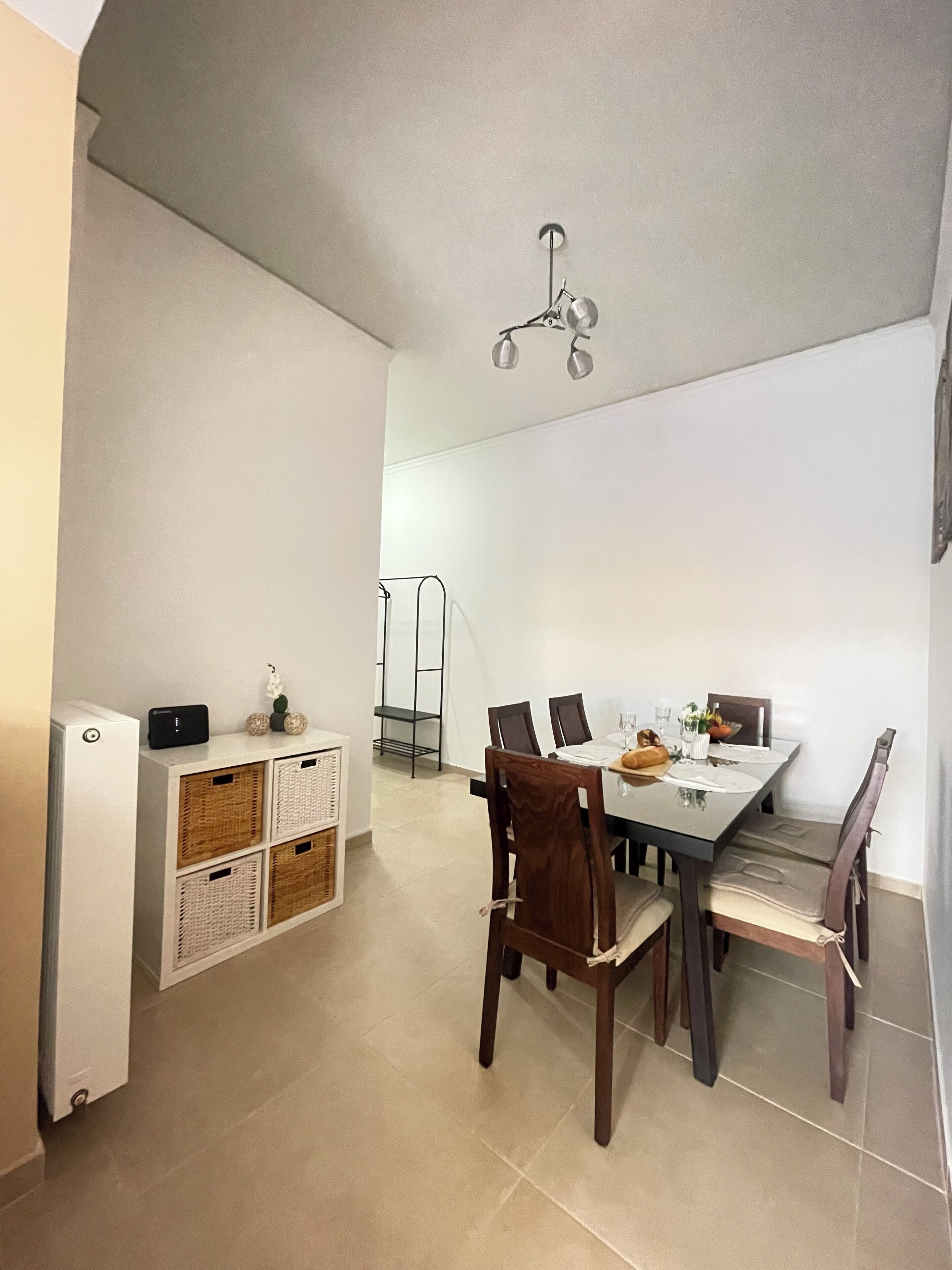 A dining area with a table set for four, a white refrigerator, wicker baskets, and a ceiling light fixture.