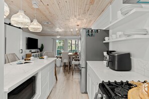 Eine moderne Küche mit weißen Schränken, einem eingebauten Backofen, einem Gasherd und einer Kaffeemaschine. Es gibt Korbtropflichten, einen Flachbildfernseher und einen Essbereich mit Tisch und Stühlen.