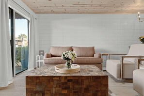 Ein modernes Wohnzimmer mit Couchtisch aus Holz, beiger Couch und Glastür zum Balkon.