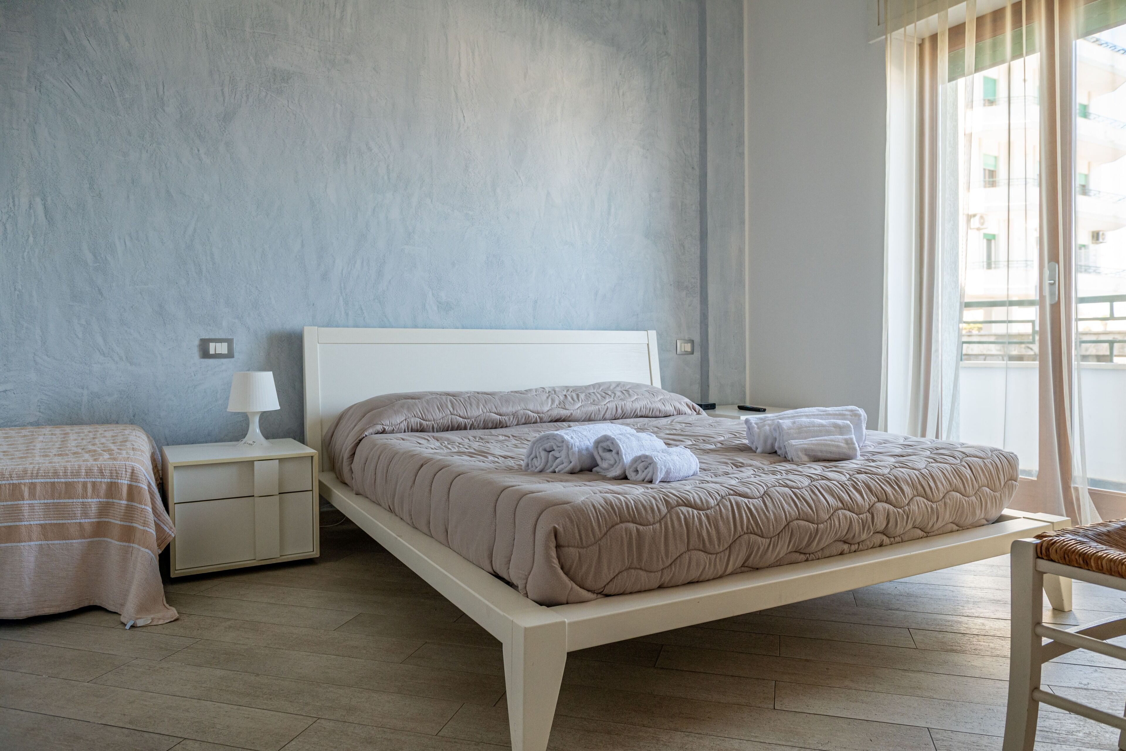 Une chambre à coucher avec un lit, une table de chevet, une lampe et une vue sur l’extérieur.
