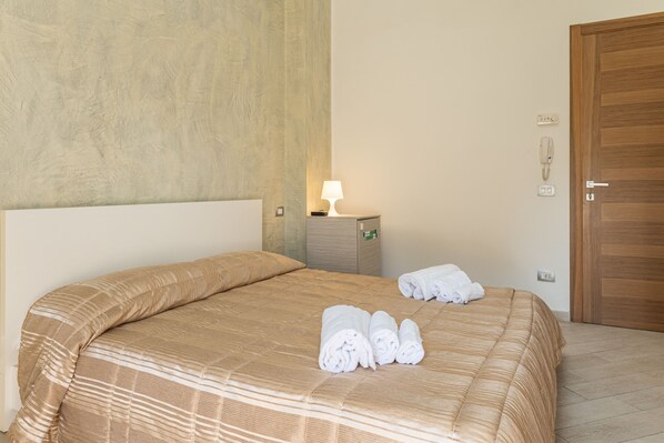 A hotel room with a large bed, a bedside lamp, a wooden door, and a small table with towels. - Hotiday Gallipoli Lungomare (Gallipoli)
