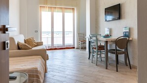 Habitación de hotel con sofá, una mesa de comedor con sillas, televisor montado en la pared y balcón con vistas.