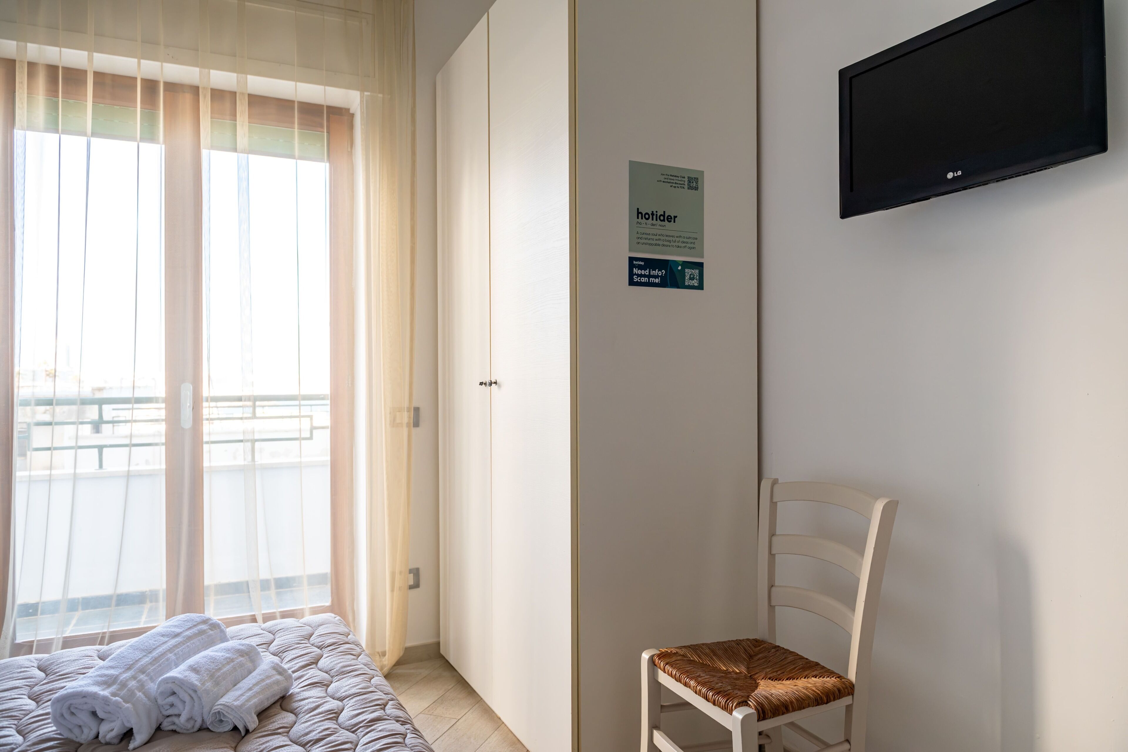 Ein Hotelzimmer mit Bett, Sessel, Kleiderschrank, Fernseher und einem Fenster mit Vorhängen.