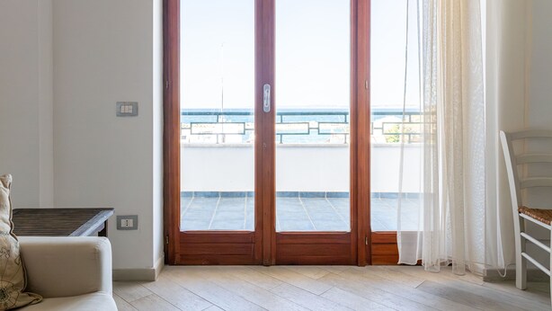 Una habitación con puerta corrediza de vidrio que da a un balcón con vista al mar.