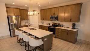 A modern kitchen with a central island, stainless steel appliances, and wooden cabinets. - The Mustang Collection 49 Newly Built Desert Retreat (Page)