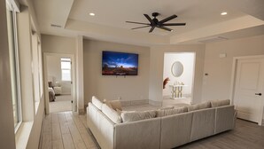 A spacious bedroom with a large bed, a ceiling fan, a TV, and a bathroom with a mirror and sink. - The Mustang Collection 49 Newly Built Desert Retreat (Page)