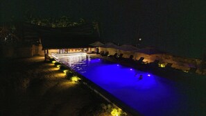 A nighttime swimming pool with a thatched-roof structure and lounge chairs. - Duli Beach Farm Hostel (El Nido)