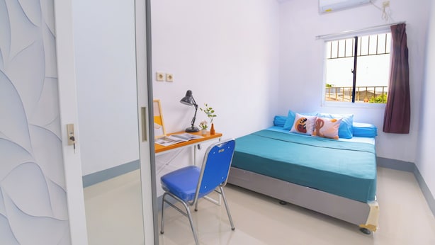 Un dormitorio con cama, escritorio, silla y ventana con cortinas.