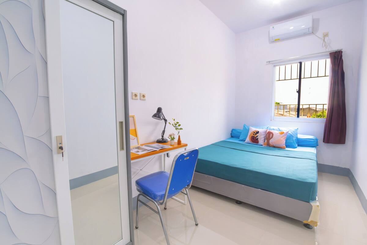 A bedroom with a bed, desk, chair, and a window with curtains.