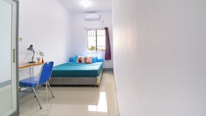 Una habitación pequeña y limpia con una cama, un escritorio y una silla. Hay una ventana con cortina y un equipo de aire acondicionado en la pared.