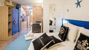 A hotel room with a bed, a blue headboard, a wall-mounted starfish decoration, a minibar, and a view of the kitchen and living area. - Elegant Ground-Floor Apartment in Porto Cesareo – Design moderno Vicino al mare (Porto Cesareo)