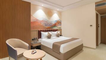 A hotel room with a bed, two chairs, a small table, a nightstand, and a wall art piece.