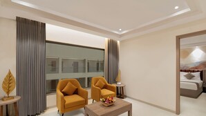 A hotel room with two armchairs, a wooden coffee table with fruit, a bed, and a large window with curtains. - Enrise By Sayaji Somnath (Veraval)