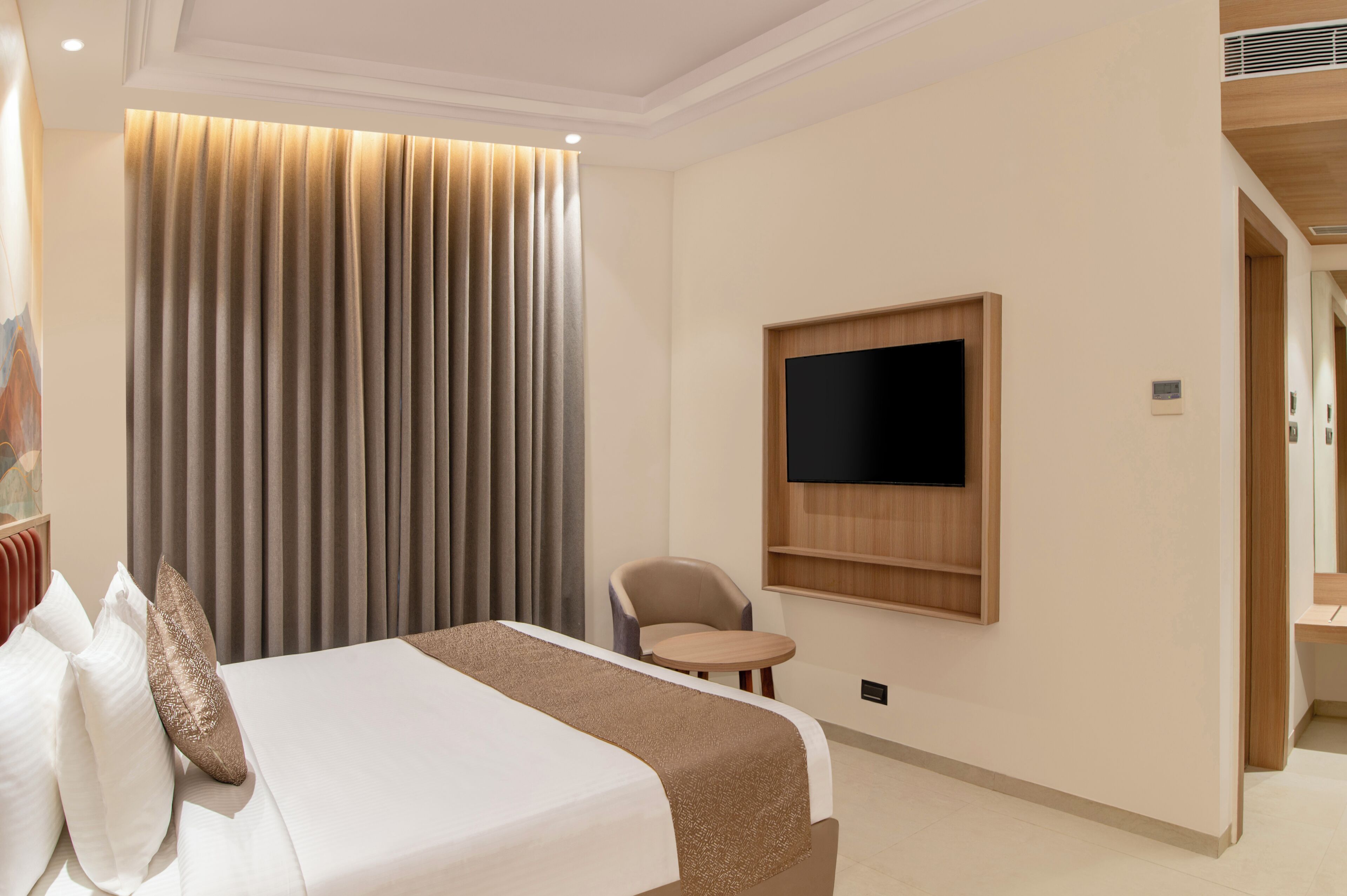Habitación de hotel con una cama, televisión instalada en la pared, una mesita pequeña y una silla.