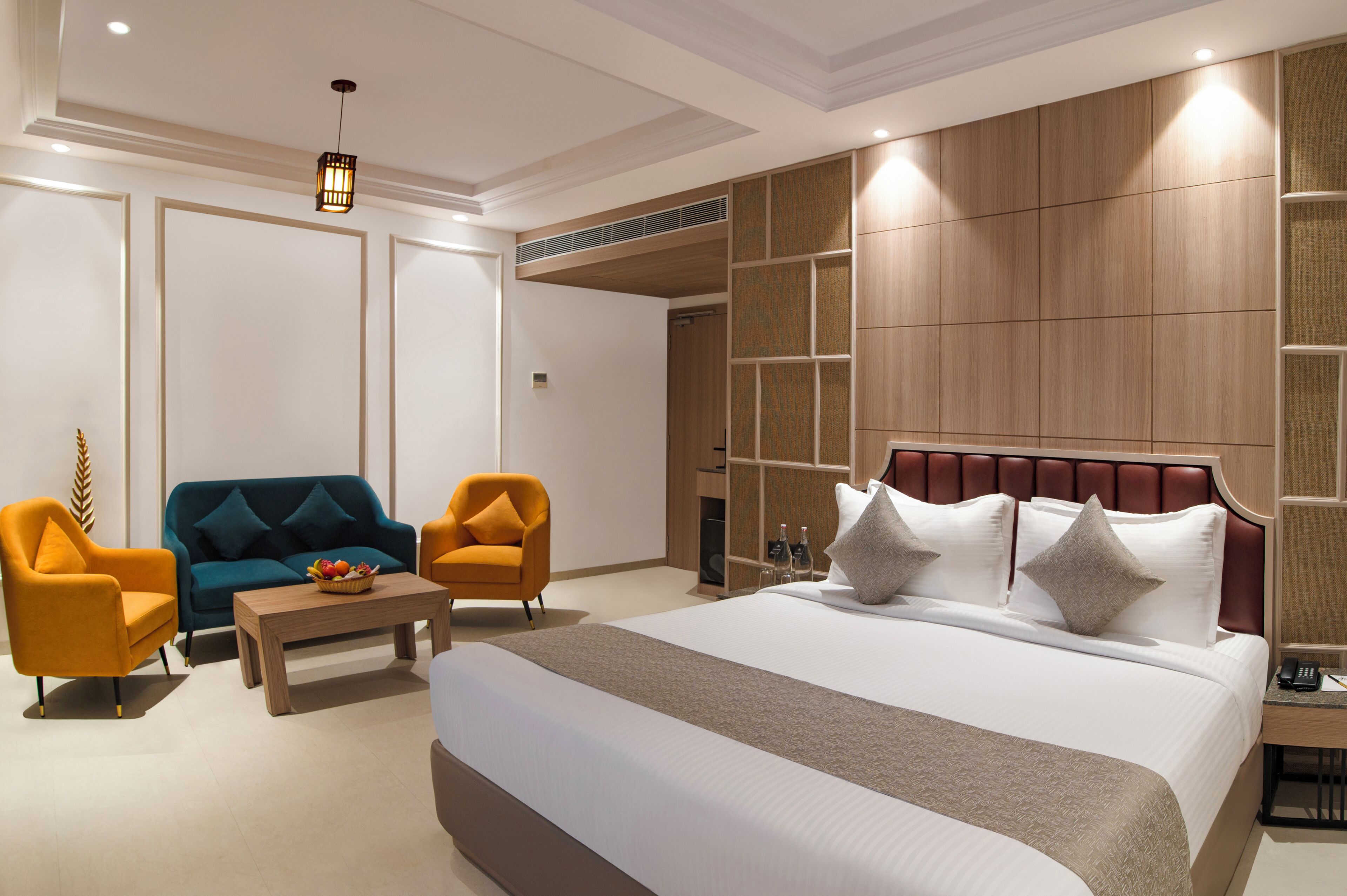 A hotel room with a large bed, two armchairs, a coffee table, and a decorative wall panel.