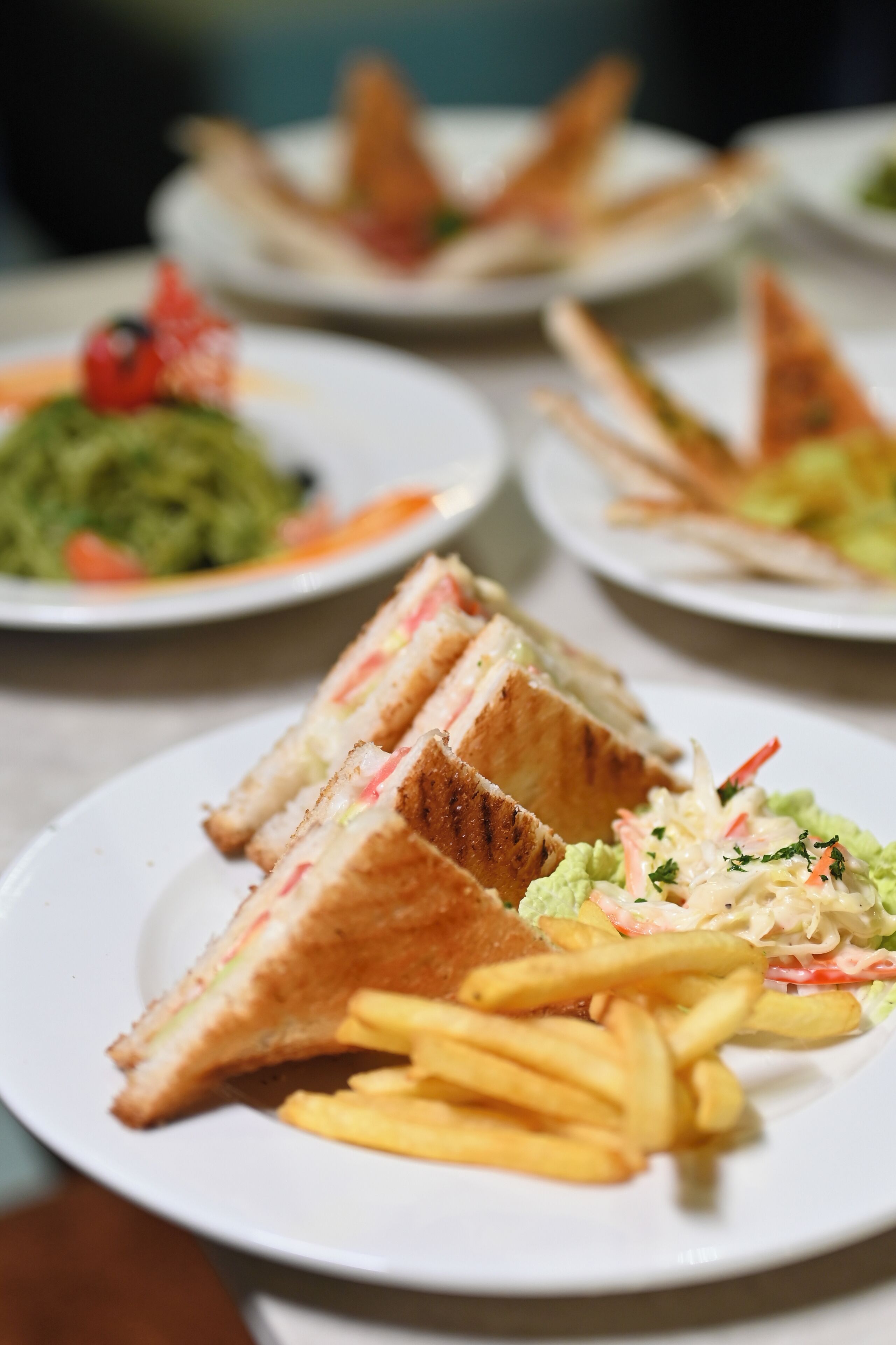 A dining table with plates of food, including sandwiches and fries.