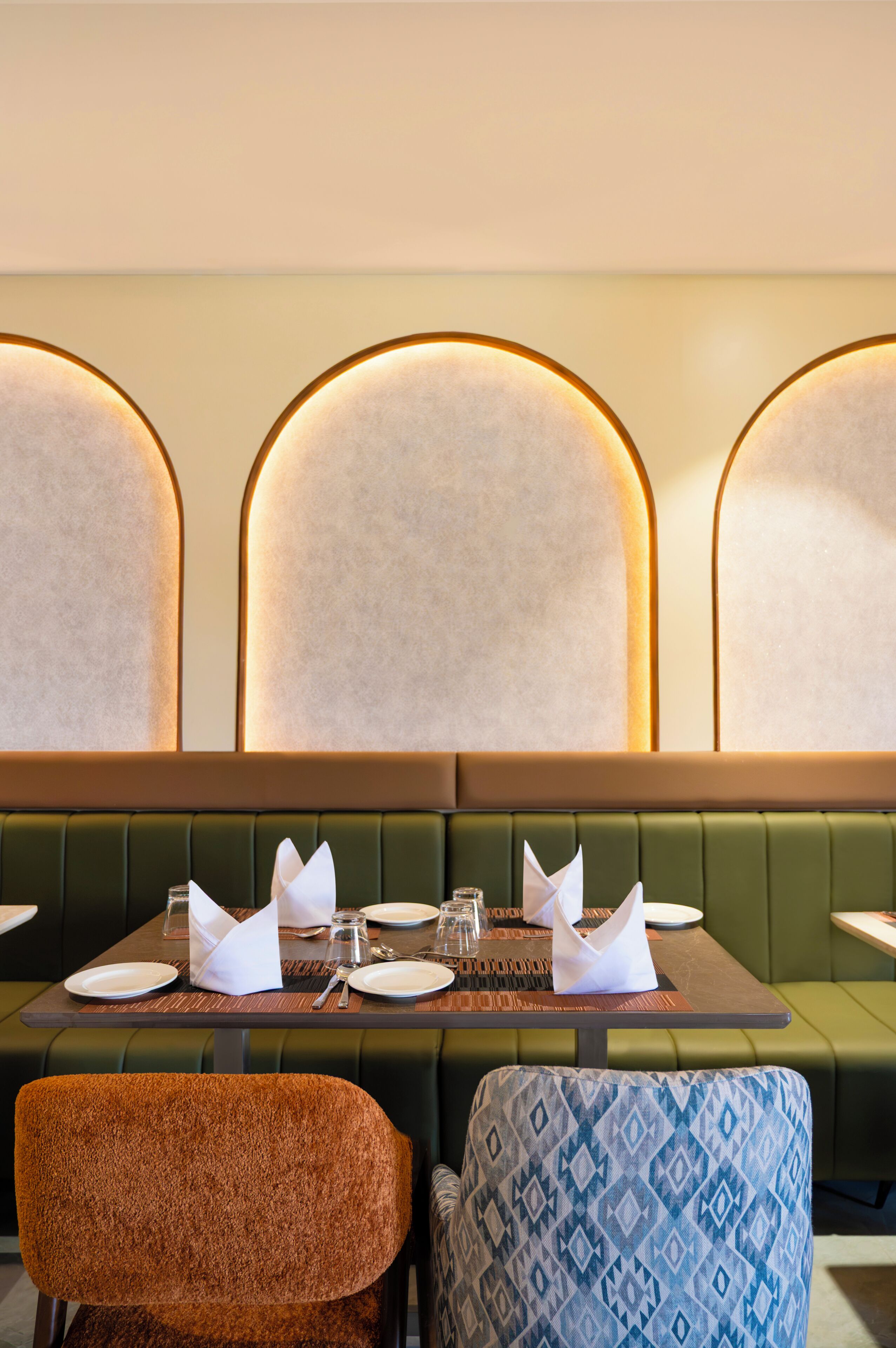 A restaurant with a green booth seating area, a table set with plates, glasses, and cutlery, and a patterned armchair.