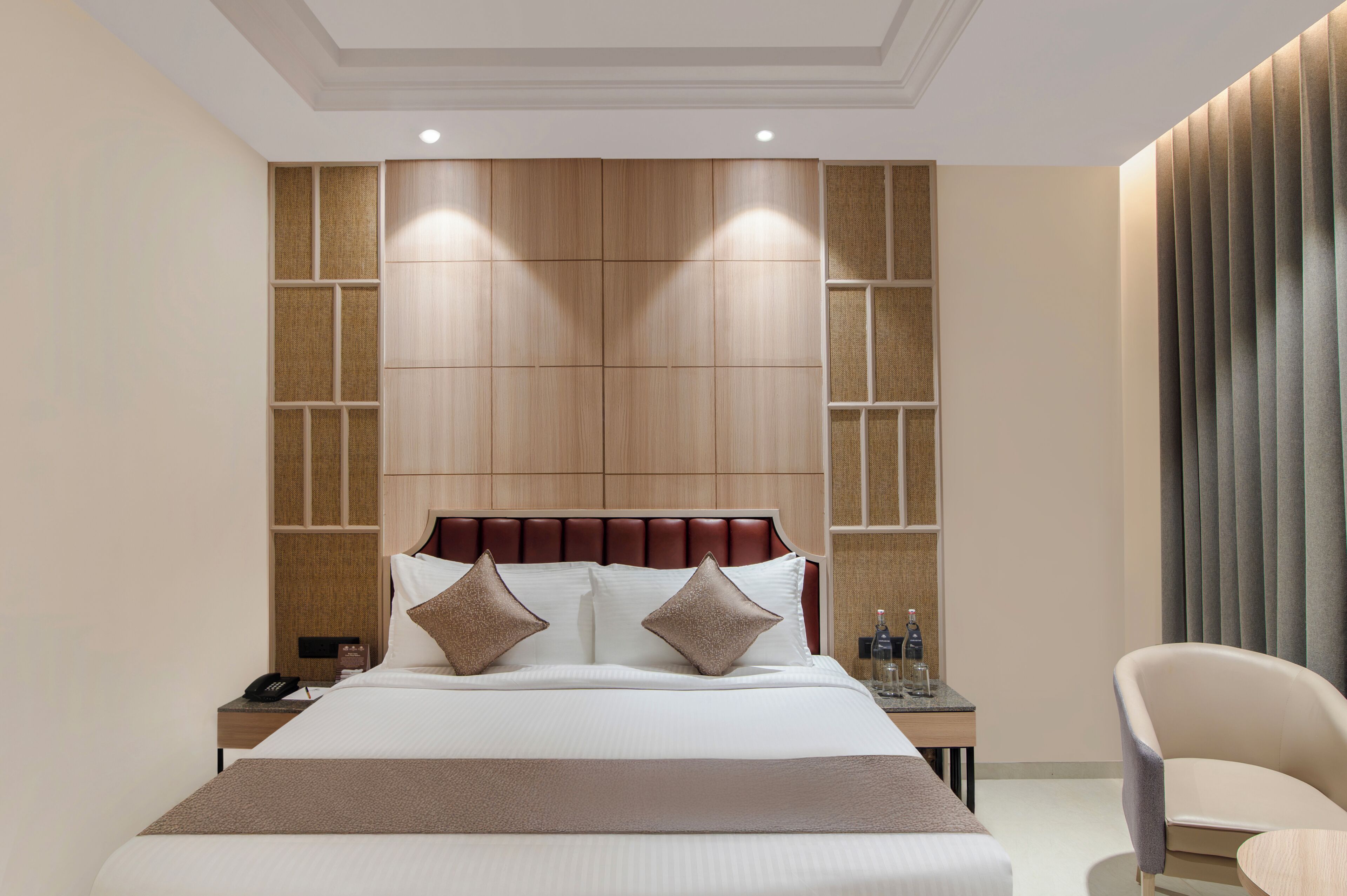 Habitación de hotel con una cama grande, una mesita de noche, una silla y un panel de madera en la pared.
