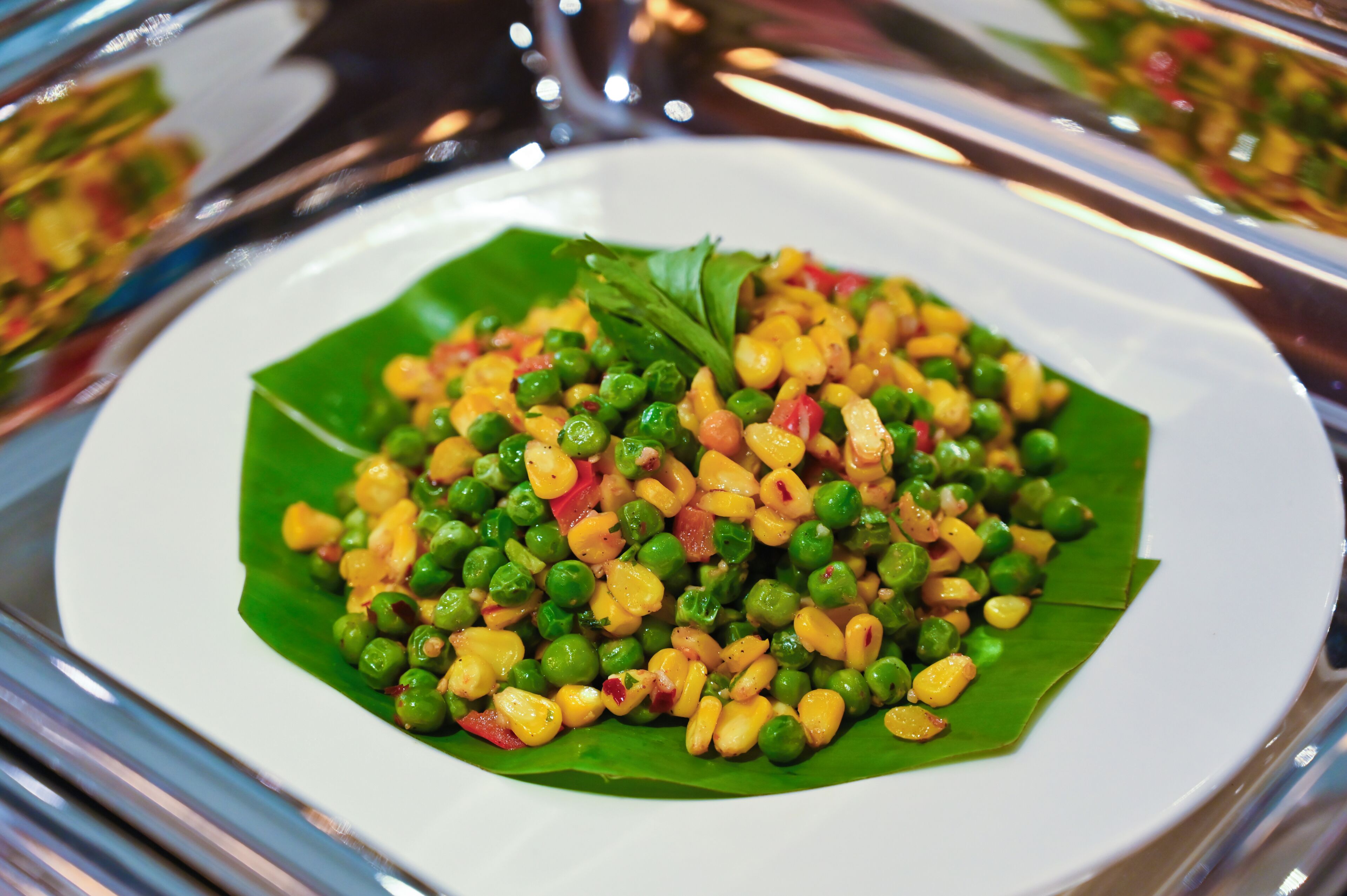 A plate of food with peas, corn, and tomatoes on a leaf.