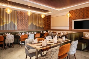 A restaurant with multiple tables and booths, equipped with napkins and cutlery. - Enrise By Sayaji Somnath (Veraval)