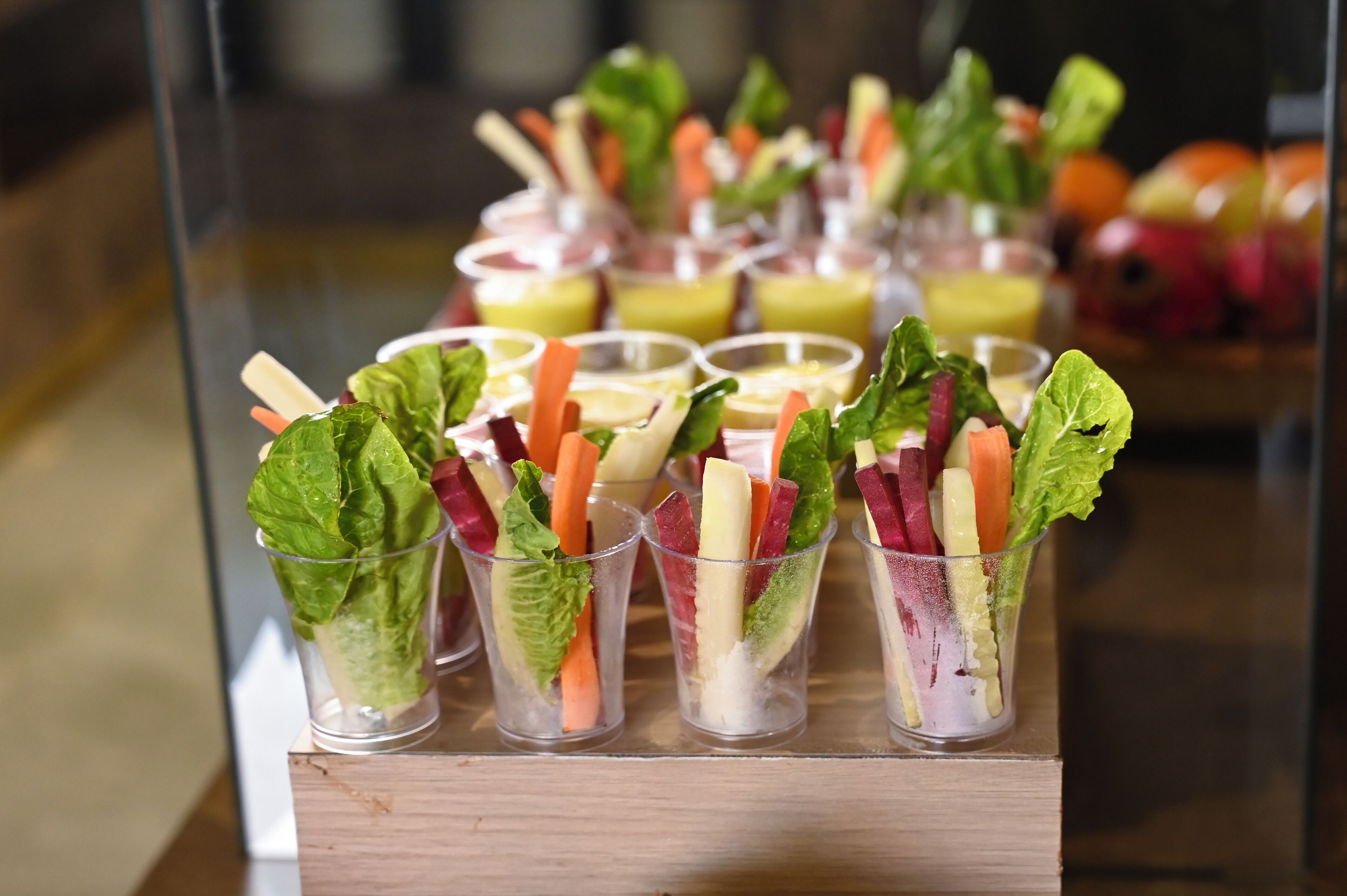 Een presentatie van glazen bekers gevuld met diverse verse groenten en fruit, gerangschikt op een houten standaard.