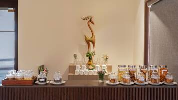 A buffet setup with various food containers, a decorative swan, and a row of white cups.