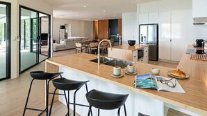 A modern kitchen with a central island, bar stools, and a dining area with a sofa and table. - NEW Luxury Hamilton Island Estate (Whitsundays)