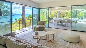 A modern living room with a large glass door leading to a balcony with a view of the sea. - NEW Luxury Hamilton Island Estate (Whitsundays)