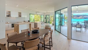 A modern kitchen with white cabinets, a wooden dining table, and wicker chairs. - NEW Luxury Hamilton Island Estate (Whitsundays)